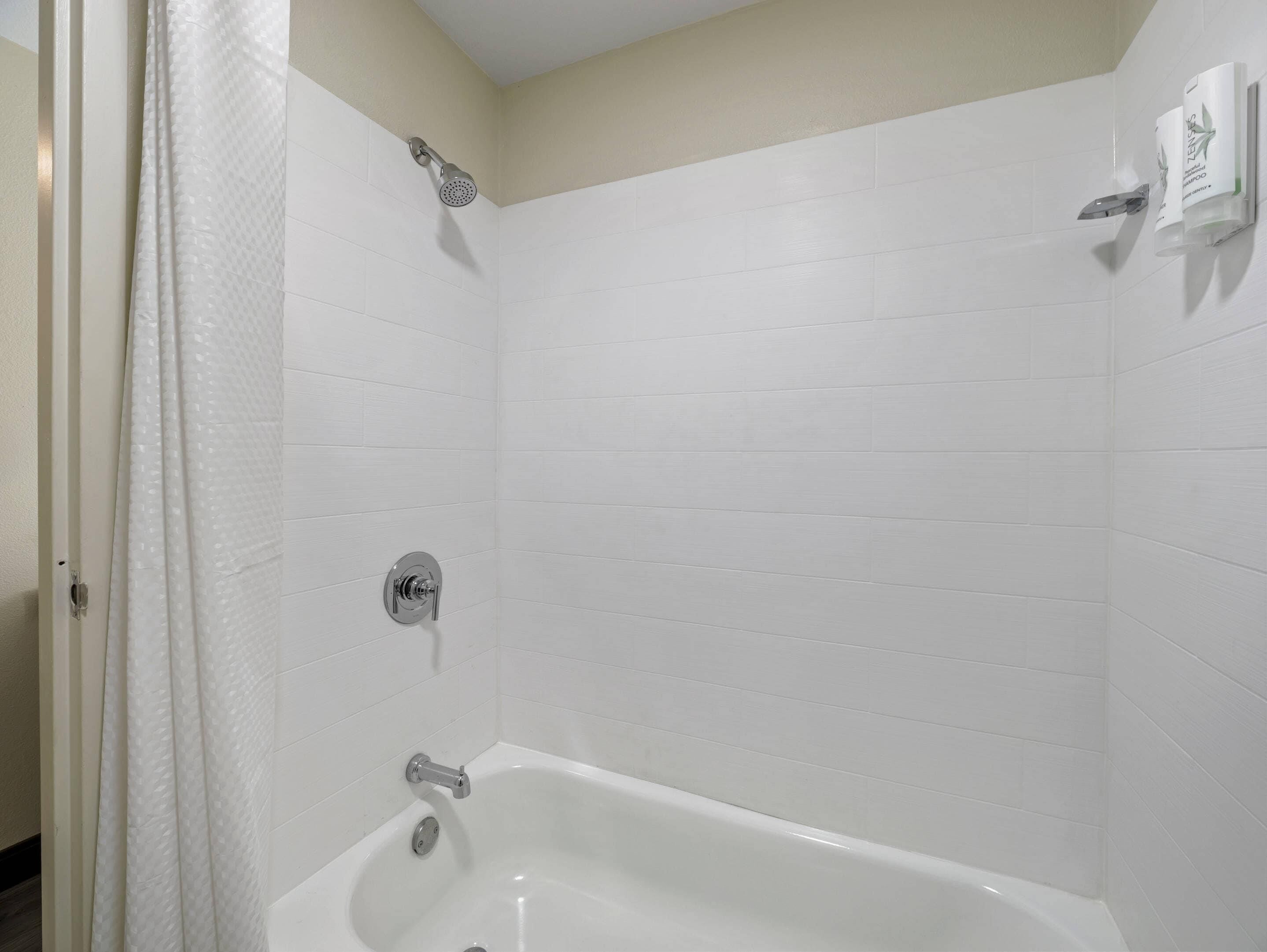 A bathroom with white tiled walls, a bathtub, a showerhead, and a toilet.