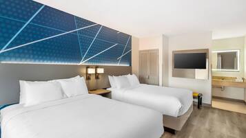 Een hotelkamer met twee bedden, een televisie, een badkamer met spiegel en een muur met een geometrisch patroon.