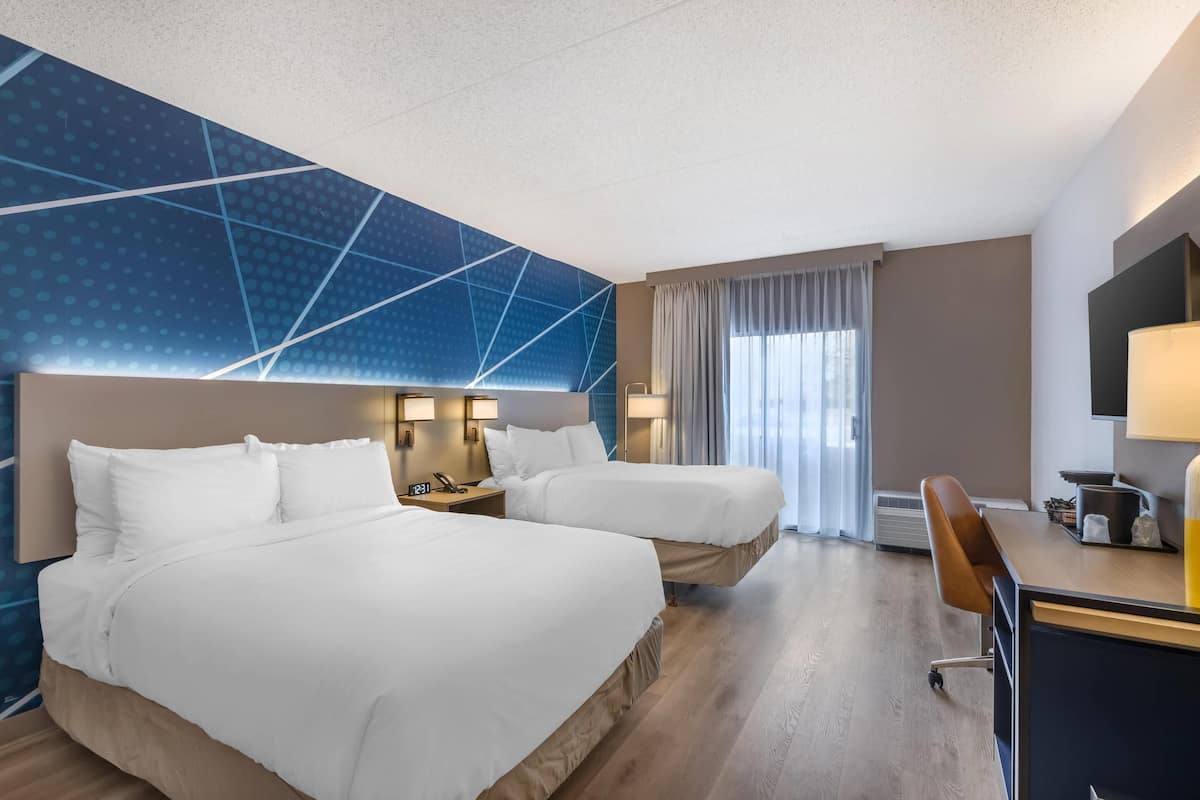 Una habitación de hotel con dos camas, un escritorio y un ventanal con cortinas.