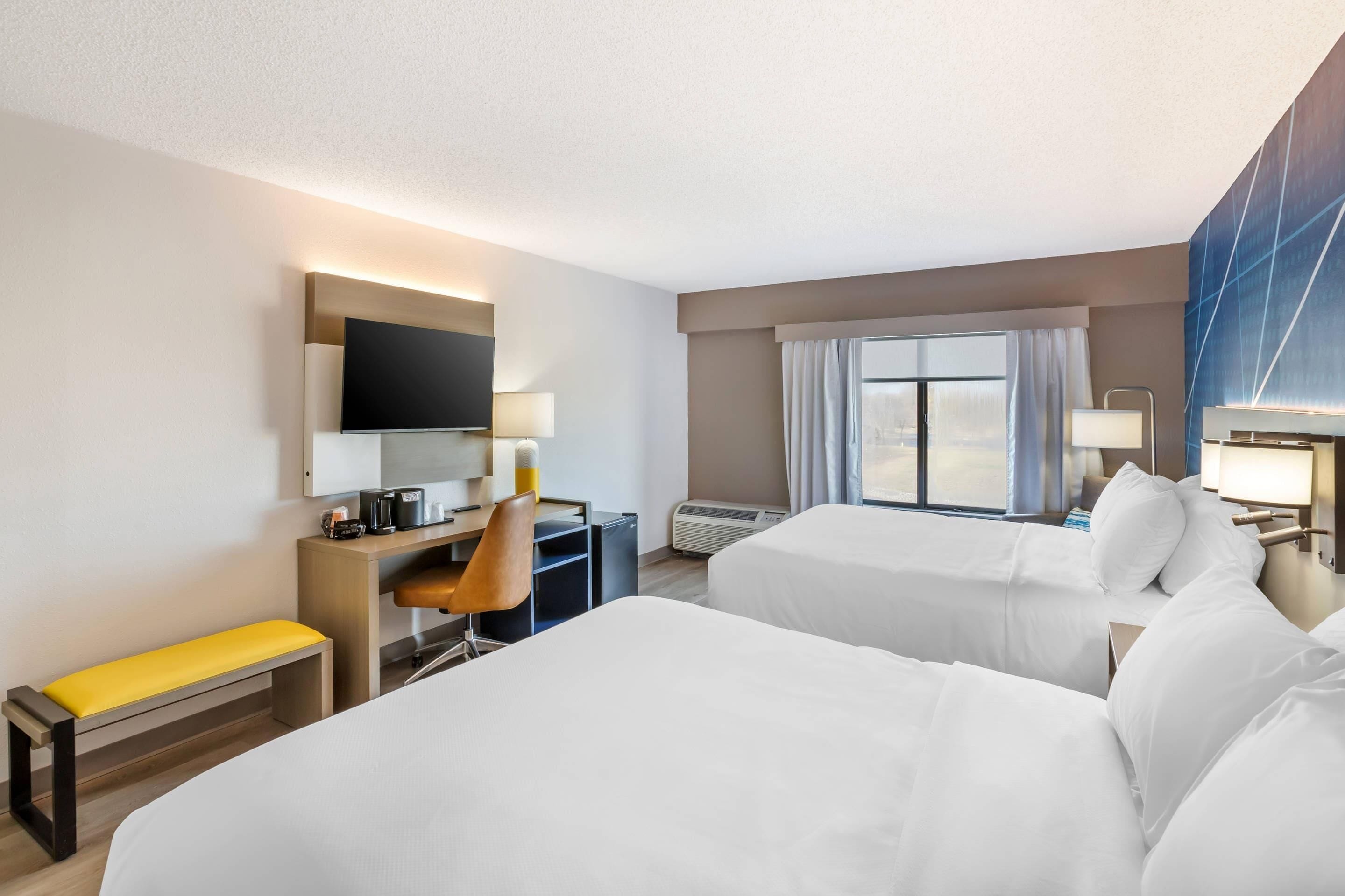 Una habitación de hotel con dos camas, un escritorio con una silla, un televisor y una ventana con cortinas.