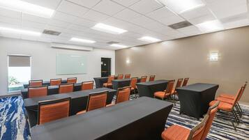 A conference room with tables and chairs, a projector screen, and a carpeted floor.