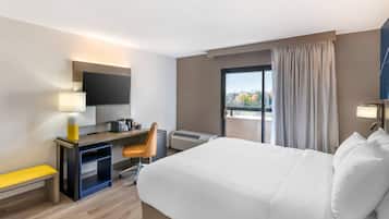 A hotel room with a bed, desk, chair, and a large window with curtains.