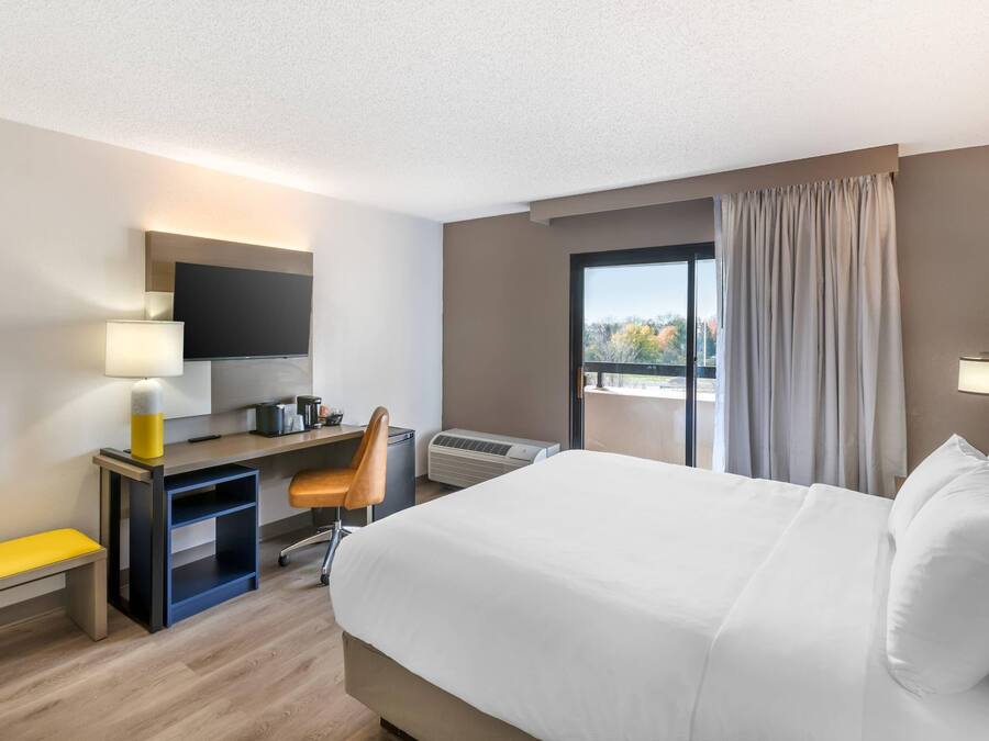 A hotel room with a bed, desk, chair, and a large window with curtains.