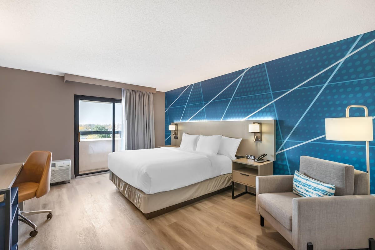 Una habitación de hotel con una cama grande, un escritorio, una silla, una mesita de noche y una lámpara.