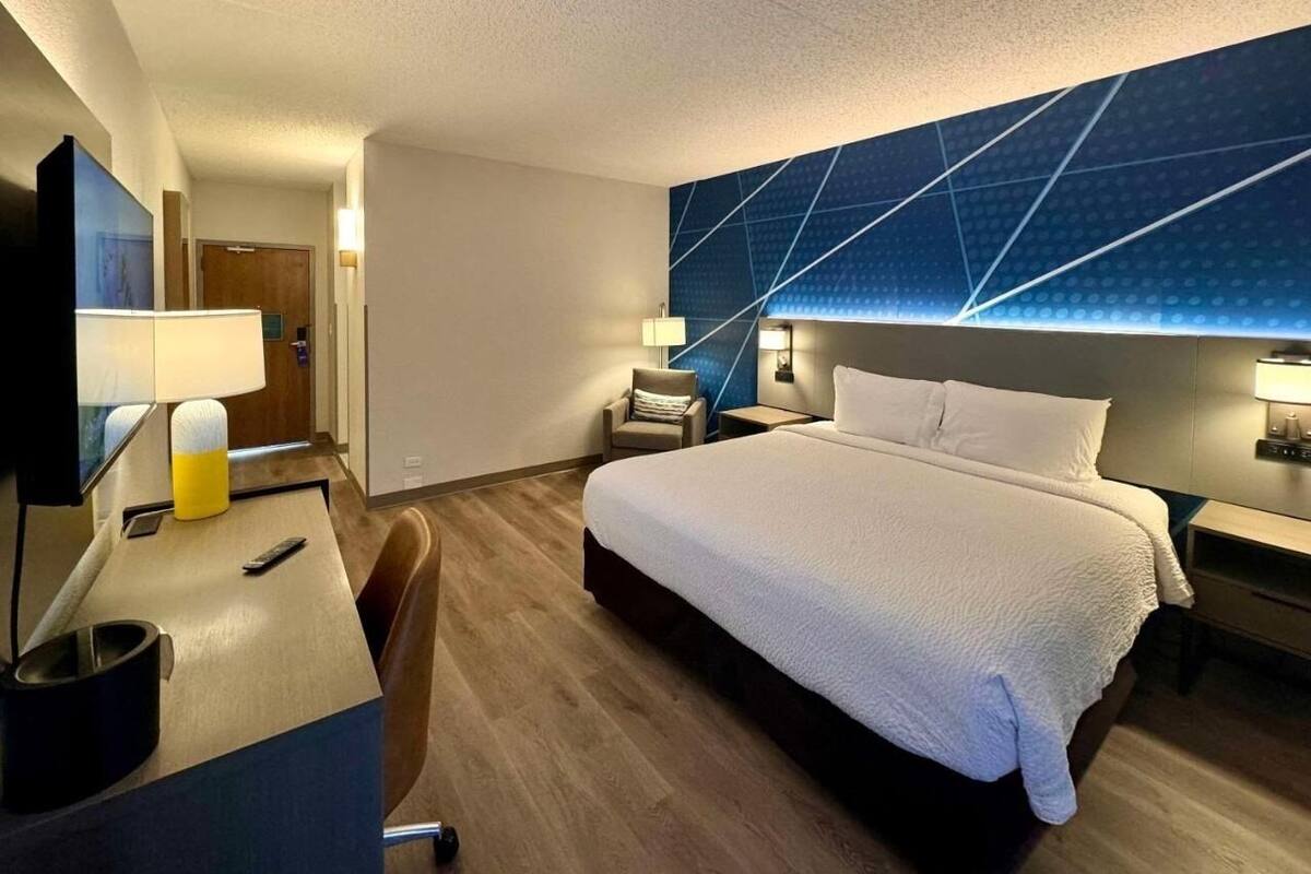 Habitación de hotel con una cama grande, un escritorio con lámpara, una silla y un televisor.