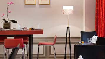 A hotel room with a dining area, a red chair, a table with a white teapot, and a floor lamp.