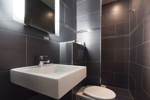A modern bathroom with a white sink, a toilet, and dark tiled walls.