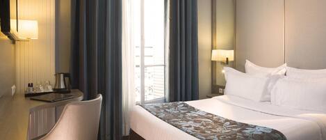 Habitación de hotel con cama, escritorio, silla, ventana con cortinas y espejo.