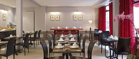 A hotel dining area with multiple tables and chairs, a buffet setup, and red curtains.
