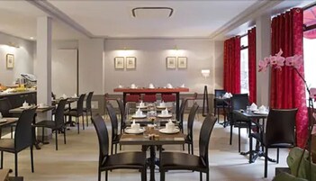 A hotel dining area with multiple tables and chairs, a buffet setup, and red curtains.