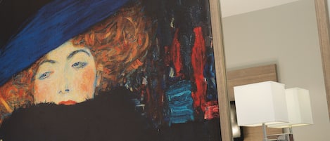 A hotel room with a large abstract painting on the wall, a modern lamp, and a wooden door.
