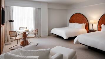 A hotel room with two beds, a desk with chairs, a TV, and a lamp.