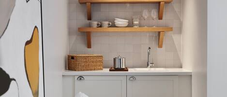 Una cocina con estantes de madera que sostienen platos y vasos, un lavabo y una cesta.
