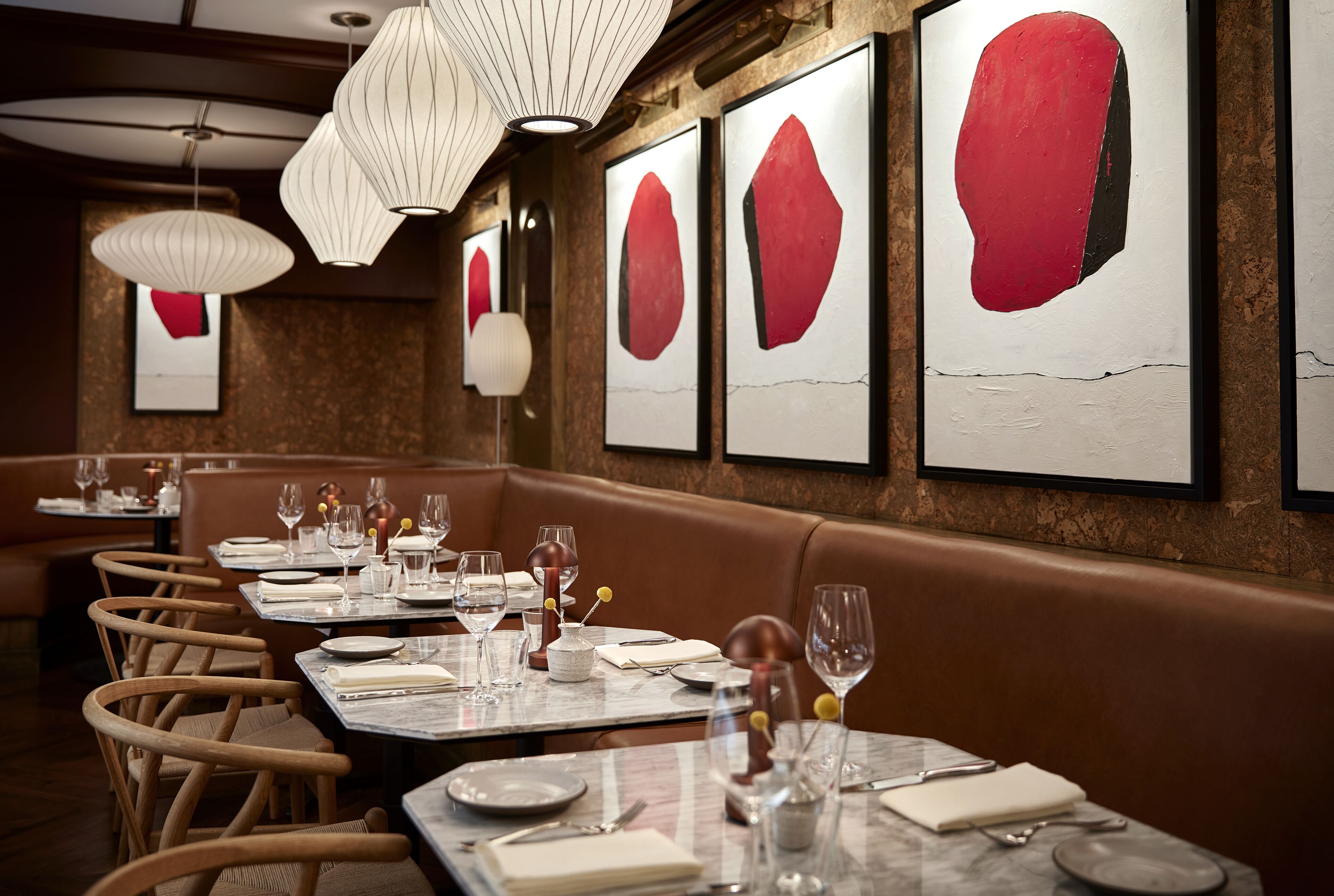 A restaurant with a long counter, wooden chairs, and tables set with plates, glasses, and cutlery.