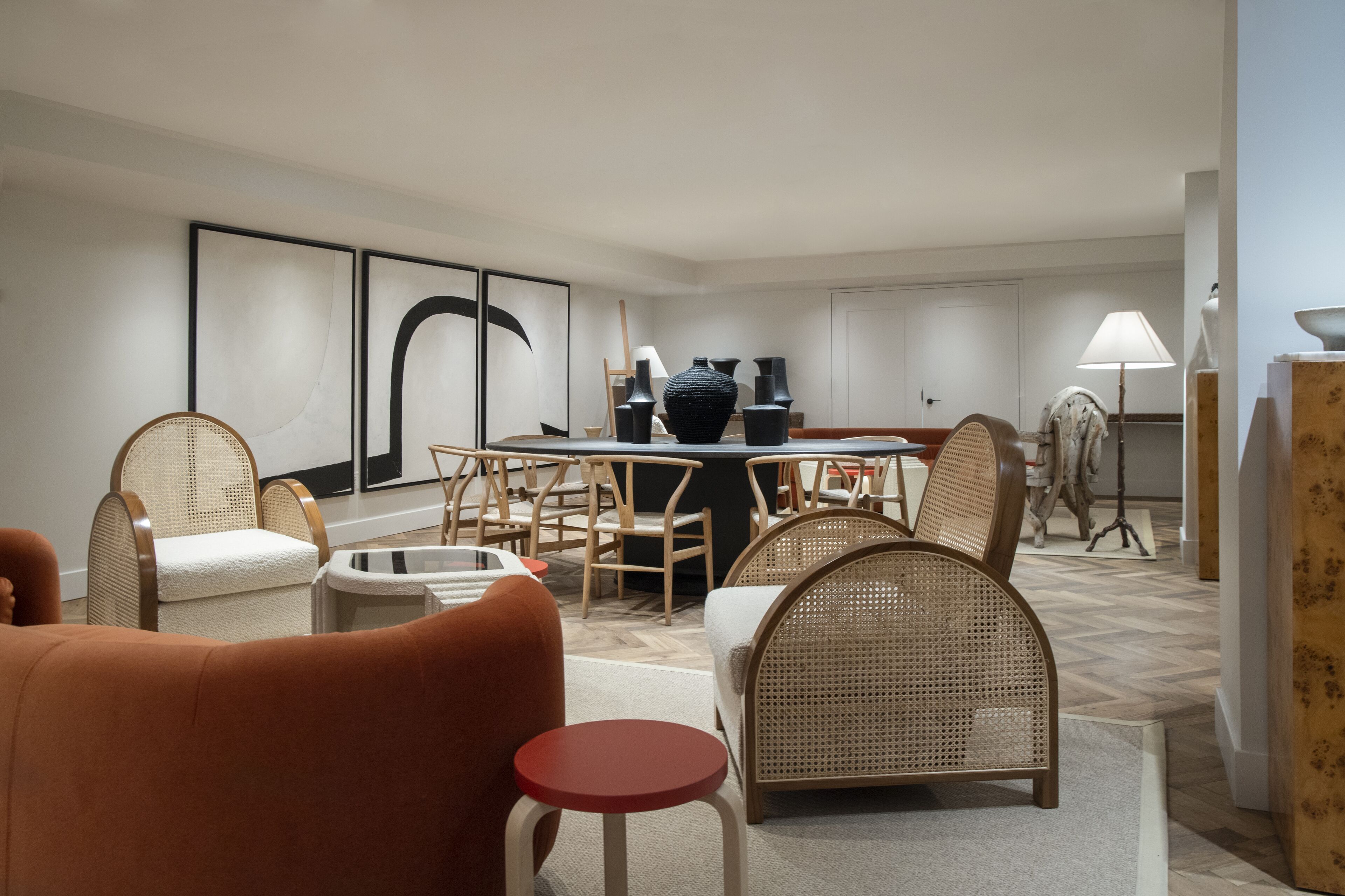A modern hotel room with a dining area, wicker furniture, and a large abstract painting on the wall.