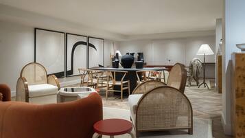 A modern hotel room with a dining area, wicker furniture, and a large abstract painting on the wall.