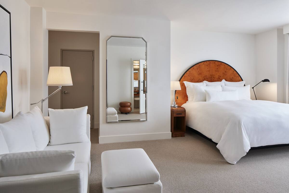 Una habitación de hotel con cama, sofá, silla, mesita y espejo.