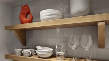 A kitchen shelf with white and red ceramic dishes, glassware, and mugs.