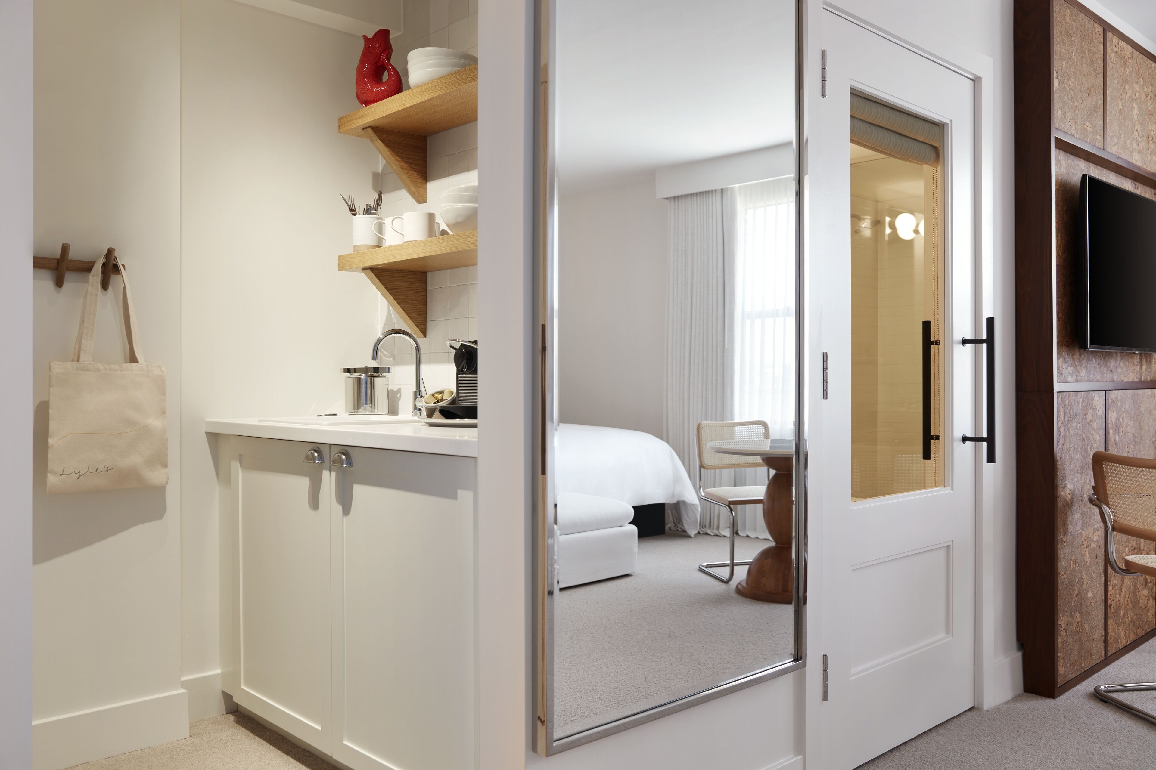 A hotel room with a white wardrobe, a mirror, a bed, a chair, and a television.