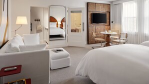 A hotel room with a large bed, a desk with a chair, a TV, and a bathroom visible through an open door.
