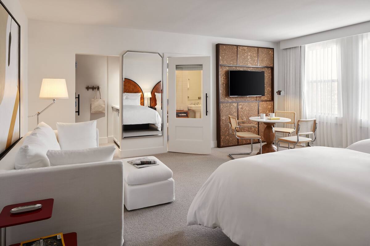 Habitación de hotel con una cama grande, un escritorio con silla, un televisor y un baño visible a través de una puerta abierta.
