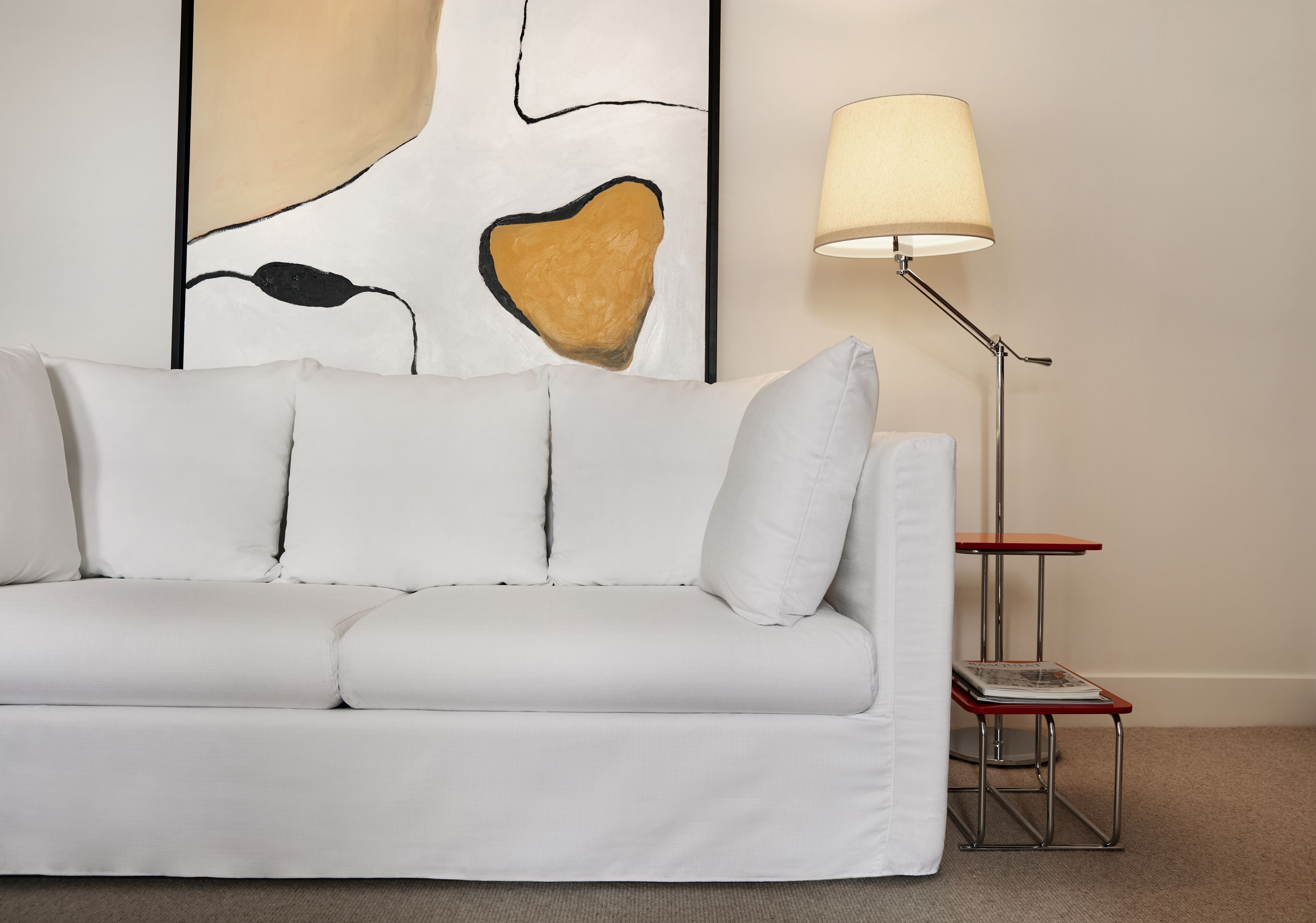 A white sofa with cushions, a floor lamp, and a small table with a magazine.