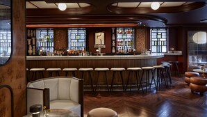 Un espace bar doté d’un comptoir incurvé, de plusieurs tabourets et d’un coin salon avec un banc rembourré et un pouf.