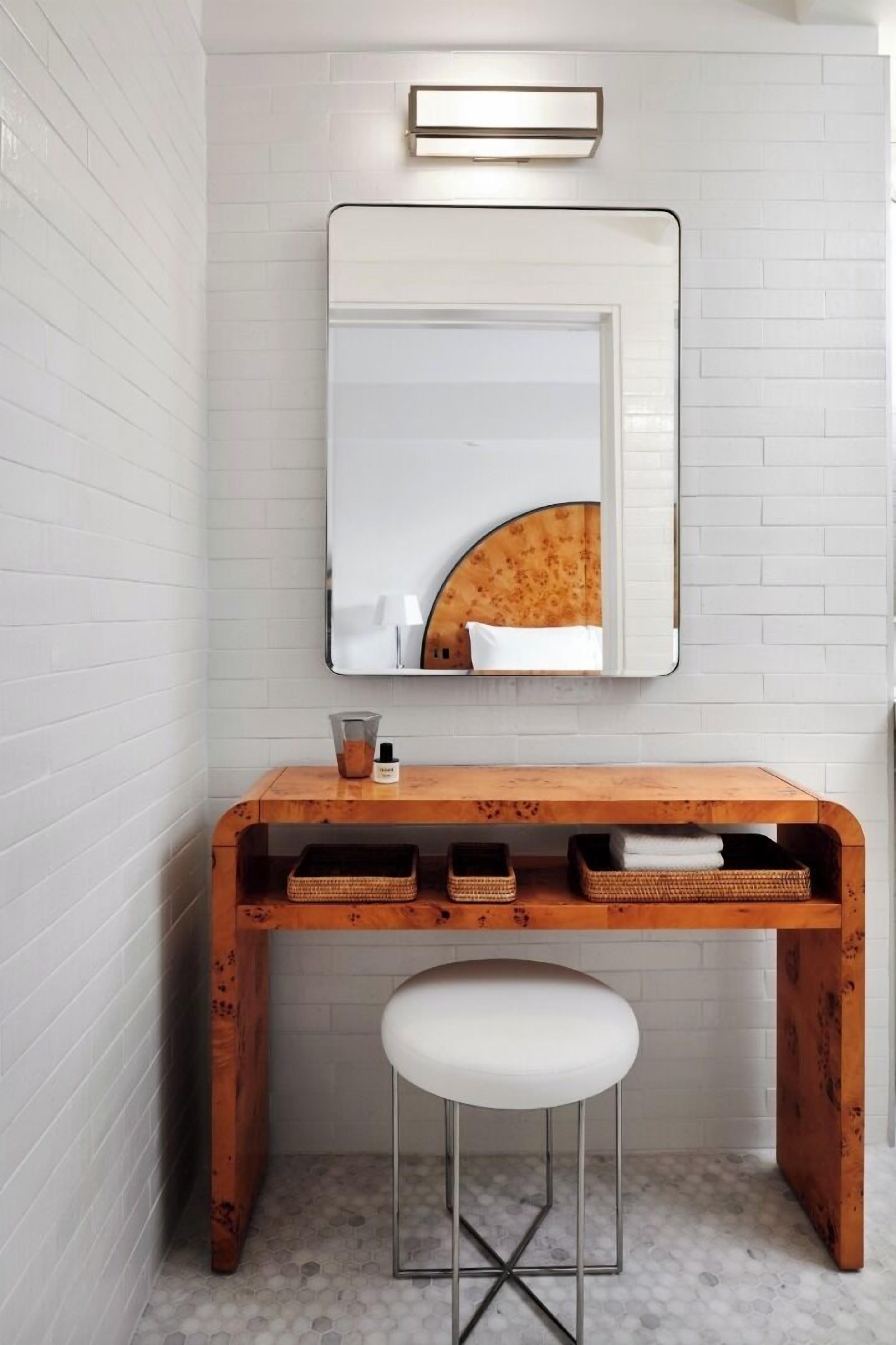 Een badkamer met een houten wastafelmeubel, een witte kruk, een spiegel met houten lijst en een lamp boven de spiegel.