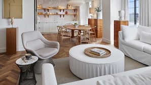 Un salon moderne avec un canapé blanc, une table basse ronde et un coin repas comprenant une table et des chaises en bois.