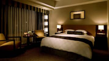A hotel room with a large bed, two bedside tables with lamps, a chair, a small table with a vase, and a window with curtains.