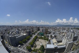A cityscape with a mix of modern and older buildings, a central roundabout, and distant mountains.