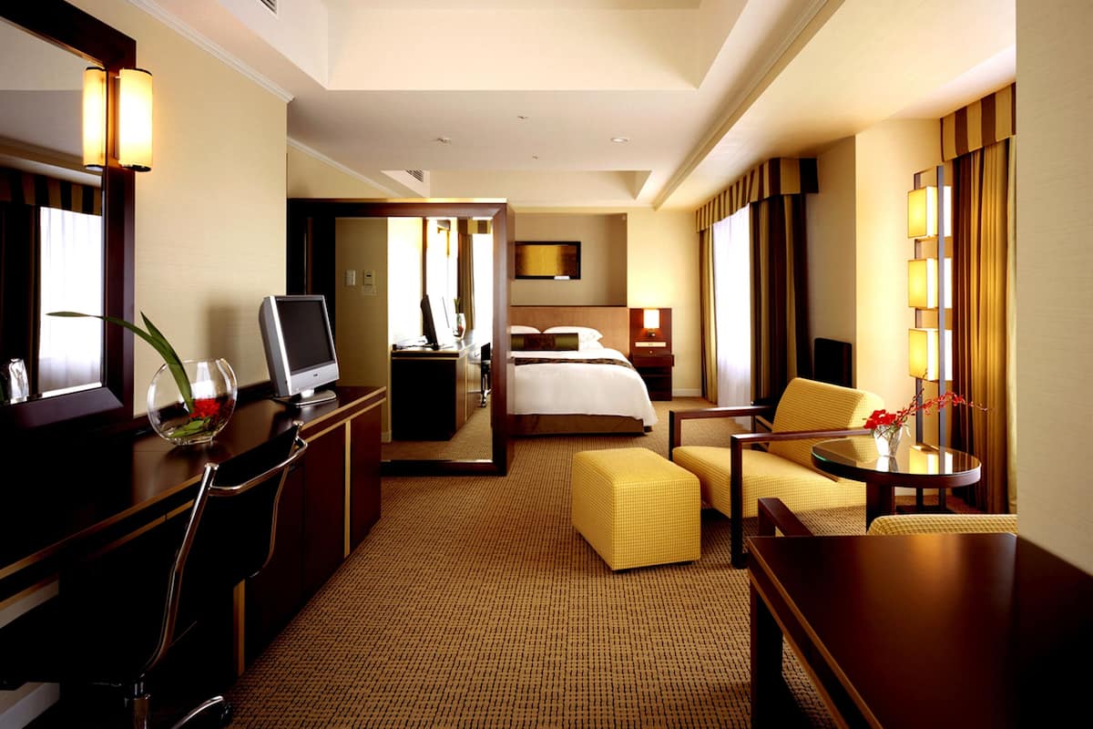 Una habitación de hotel con una cama, un escritorio con computadora, una silla, una mesita pequeña y un sofá.