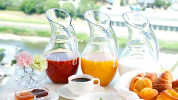 A breakfast table with various dishes, including fruit, eggs, and pastries, with a city view in the background.