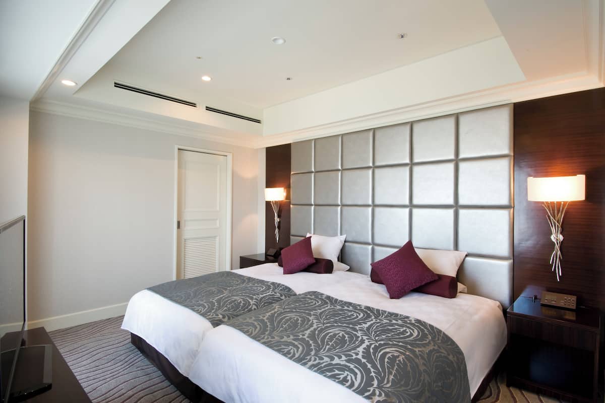 Una habitación de hotel moderna con una cama grande, un cabecero con diseño acolchado, dos lámparas de noche y un televisor de pantalla plana sobre un soporte.