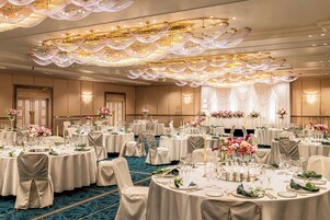 A banquet hall with round tables set for dining, chandeliers, and floral centerpieces.