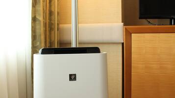 A white room heater with a control panel, a standing lamp, and a television on a wooden cabinet.