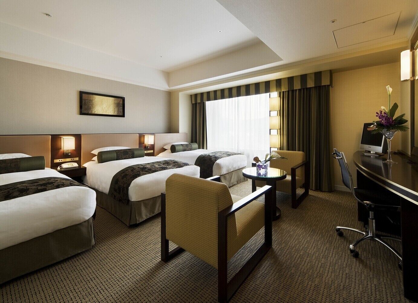 A hotel room with two beds, a desk, a chair, a small table, and a TV.