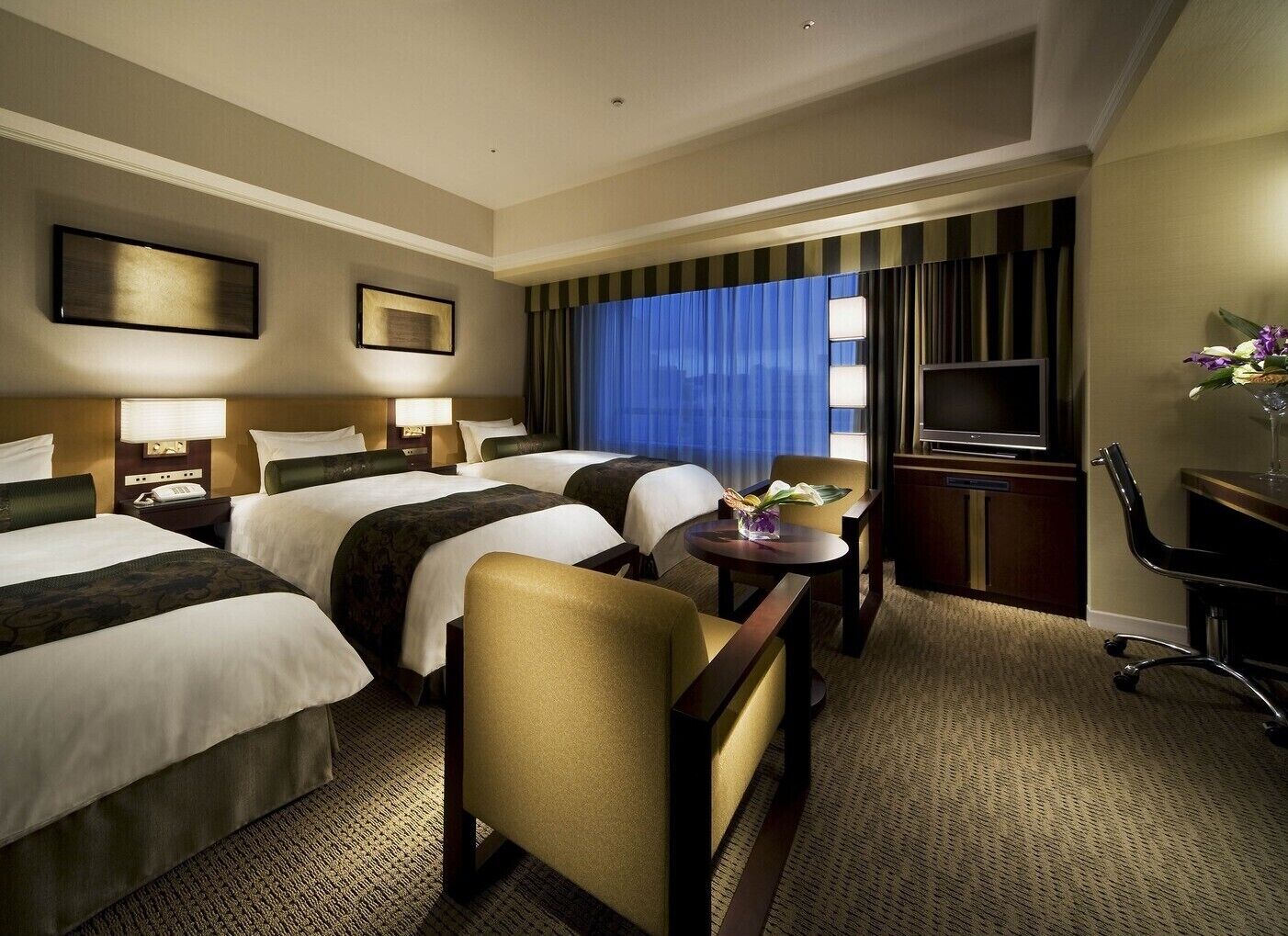 A hotel room with two beds, a desk, a chair, a television, and a window with curtains.