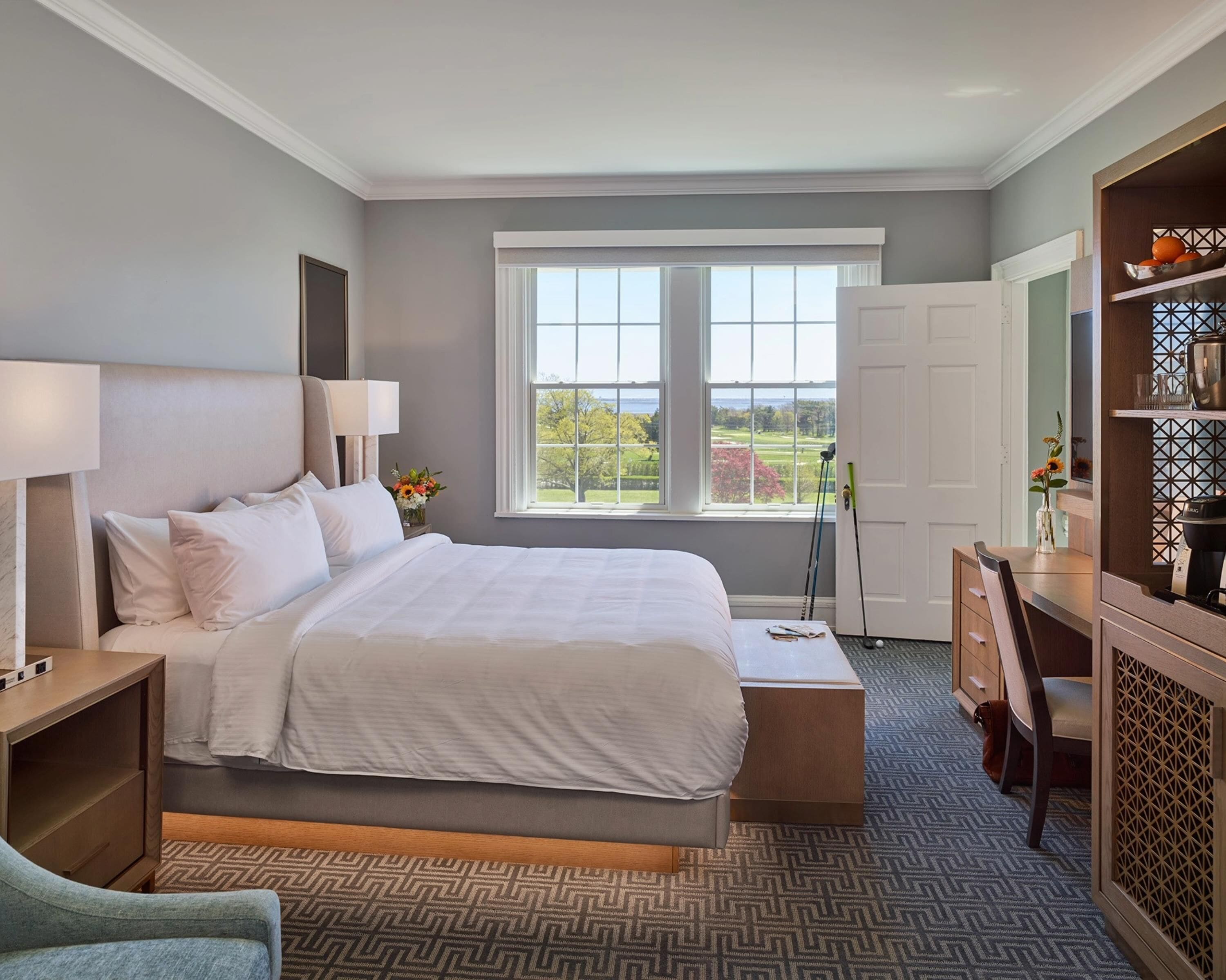 Une chambre à coucher avec un grand lit, un bureau, une chaise, une table de chevet et une fenêtre donnant sur l’extérieur.