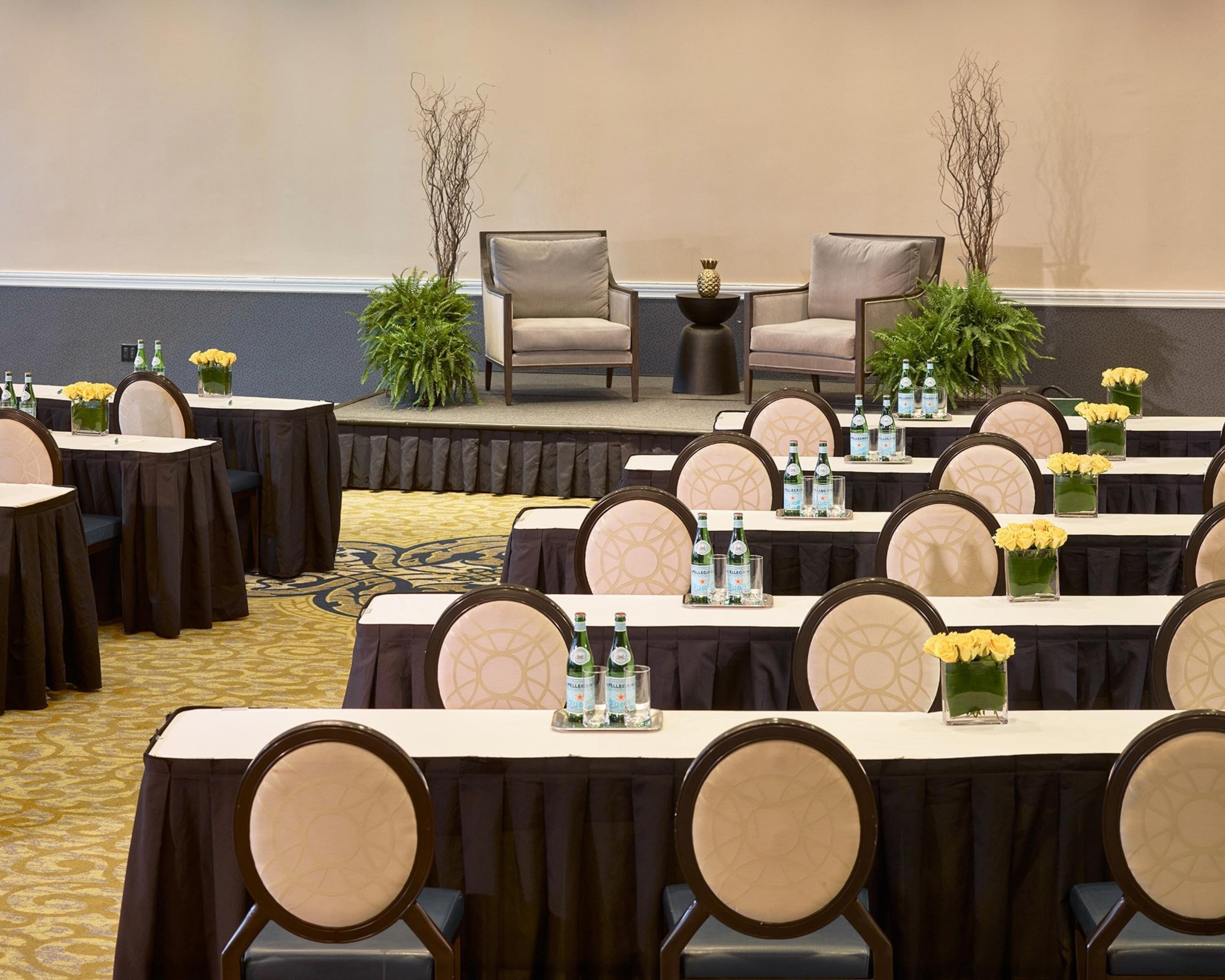 A conference room with rows of tables, chairs, and floral centerpieces.