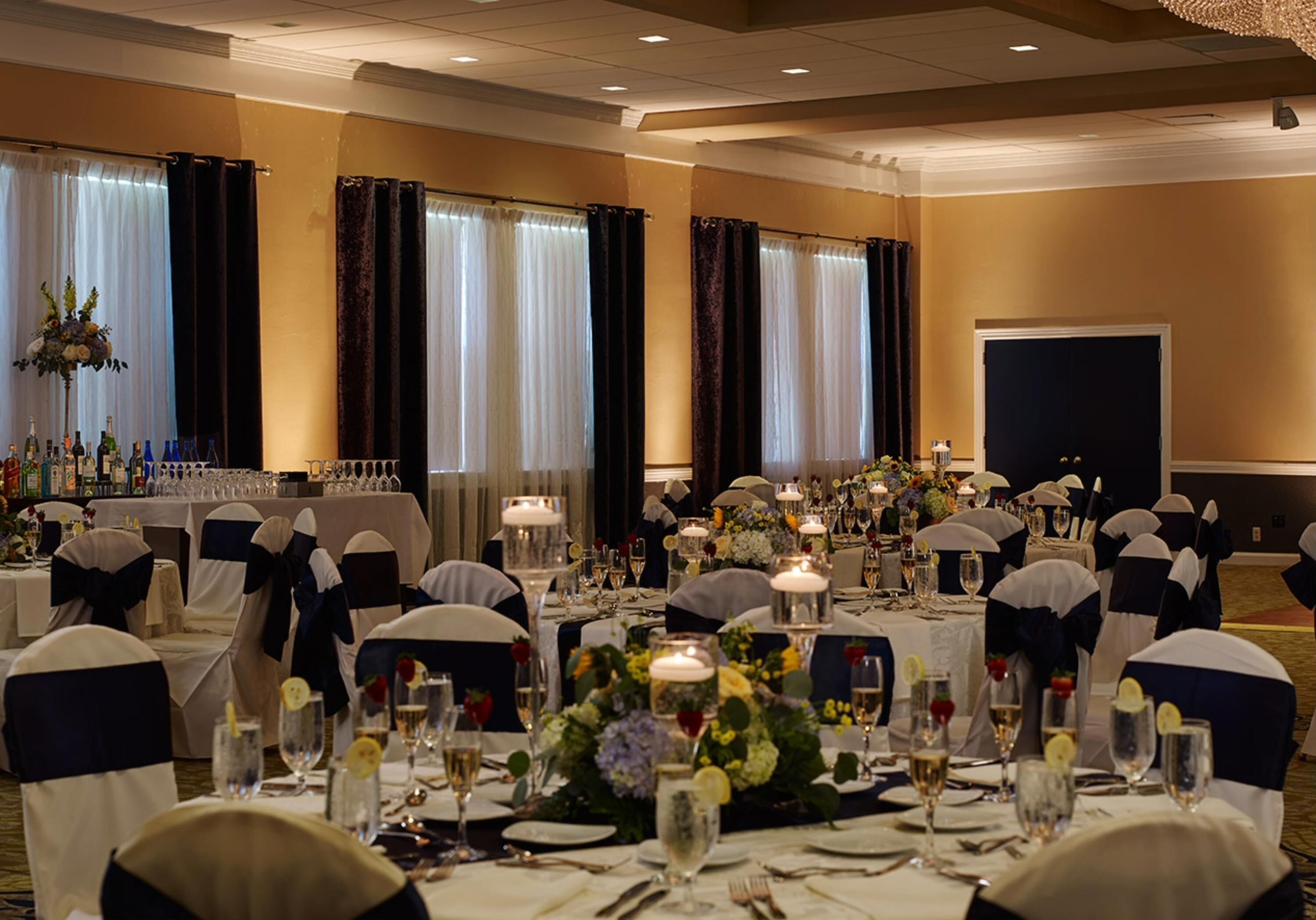 Un salón de banquetes con mesas redondas dispuestas para un evento formal, con centros de mesa florales y velas.