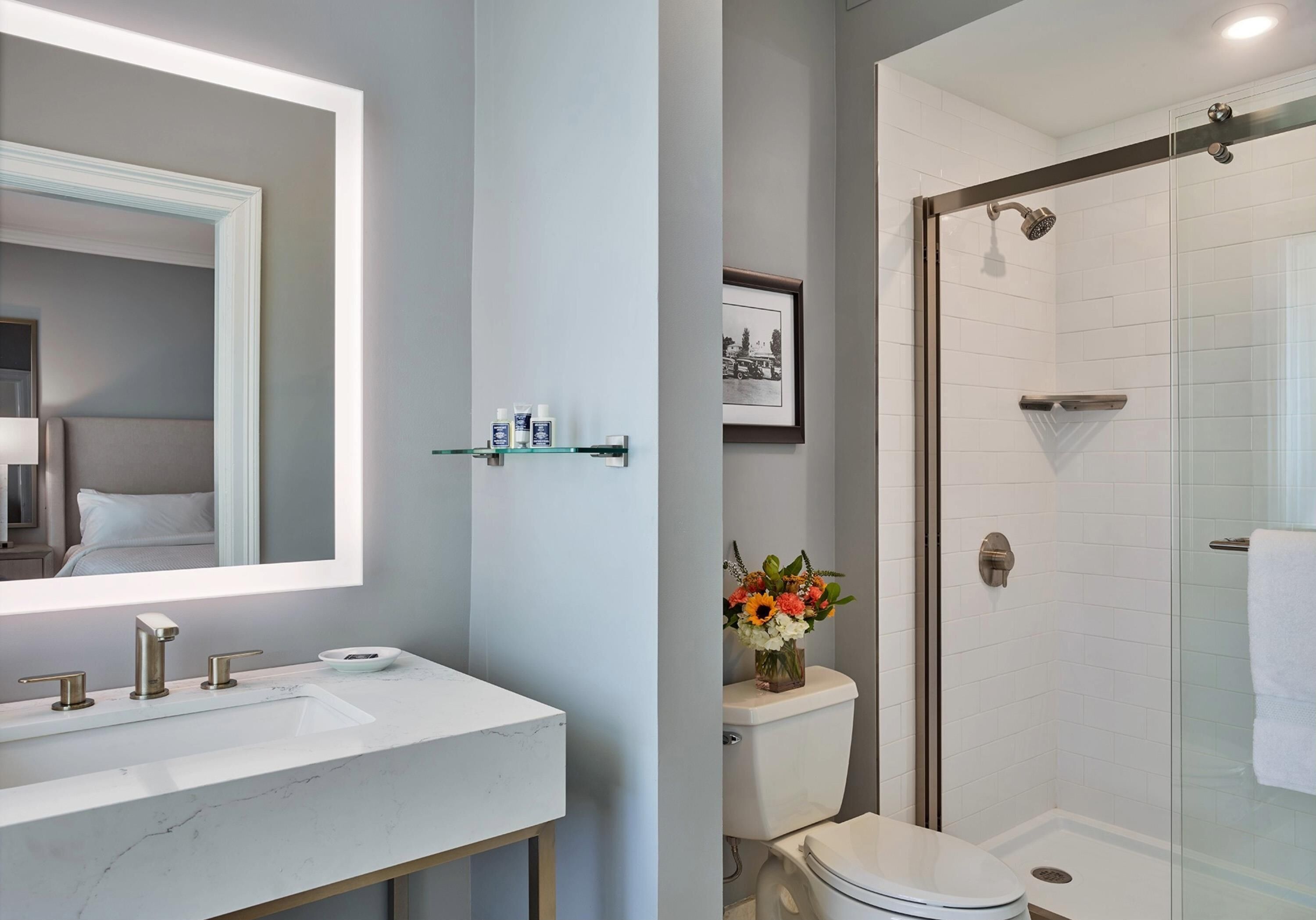 A bathroom with a large mirror, a white sink, a toilet, and a glass-enclosed shower.