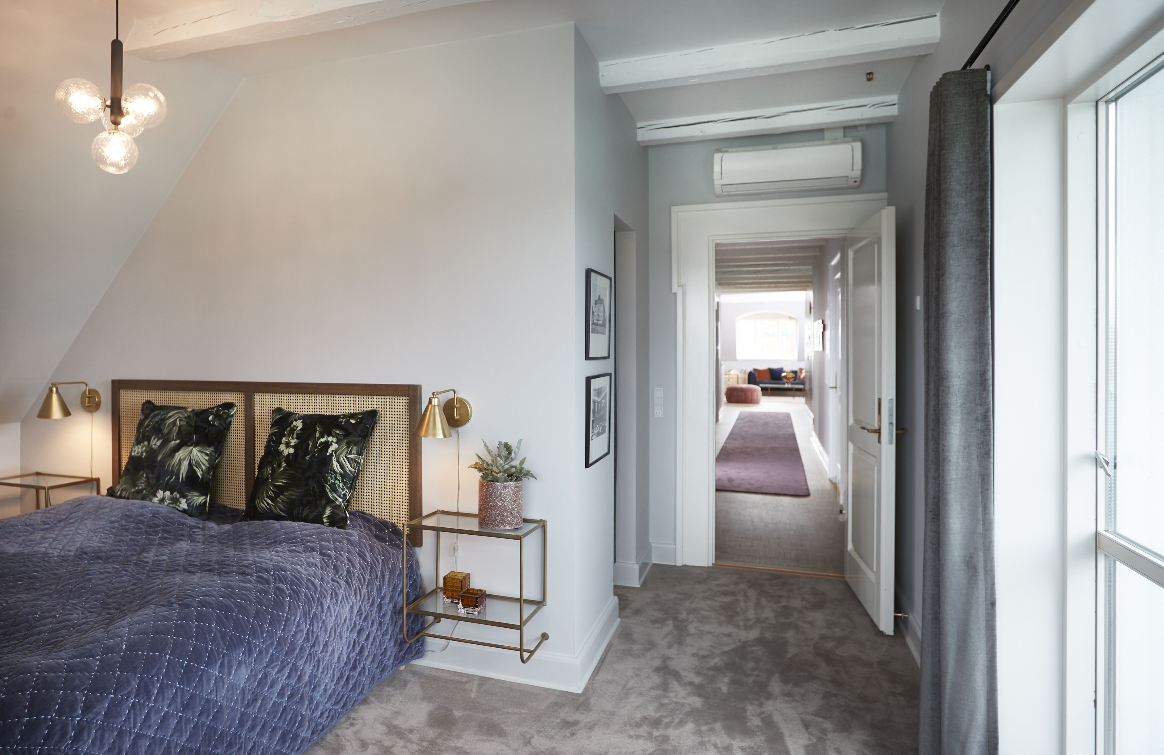 A bedroom with a bed, bedside tables, a hanging light fixture, and a door leading to another room.