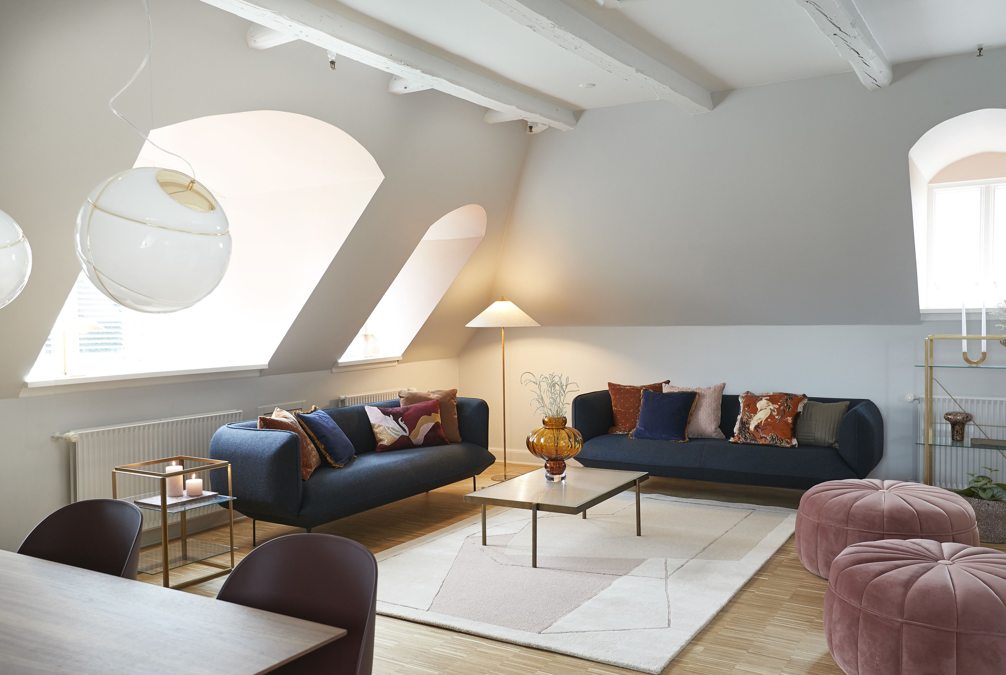 A modern living room with a sofa, coffee table, and ottoman, featuring a skylight and a large window.