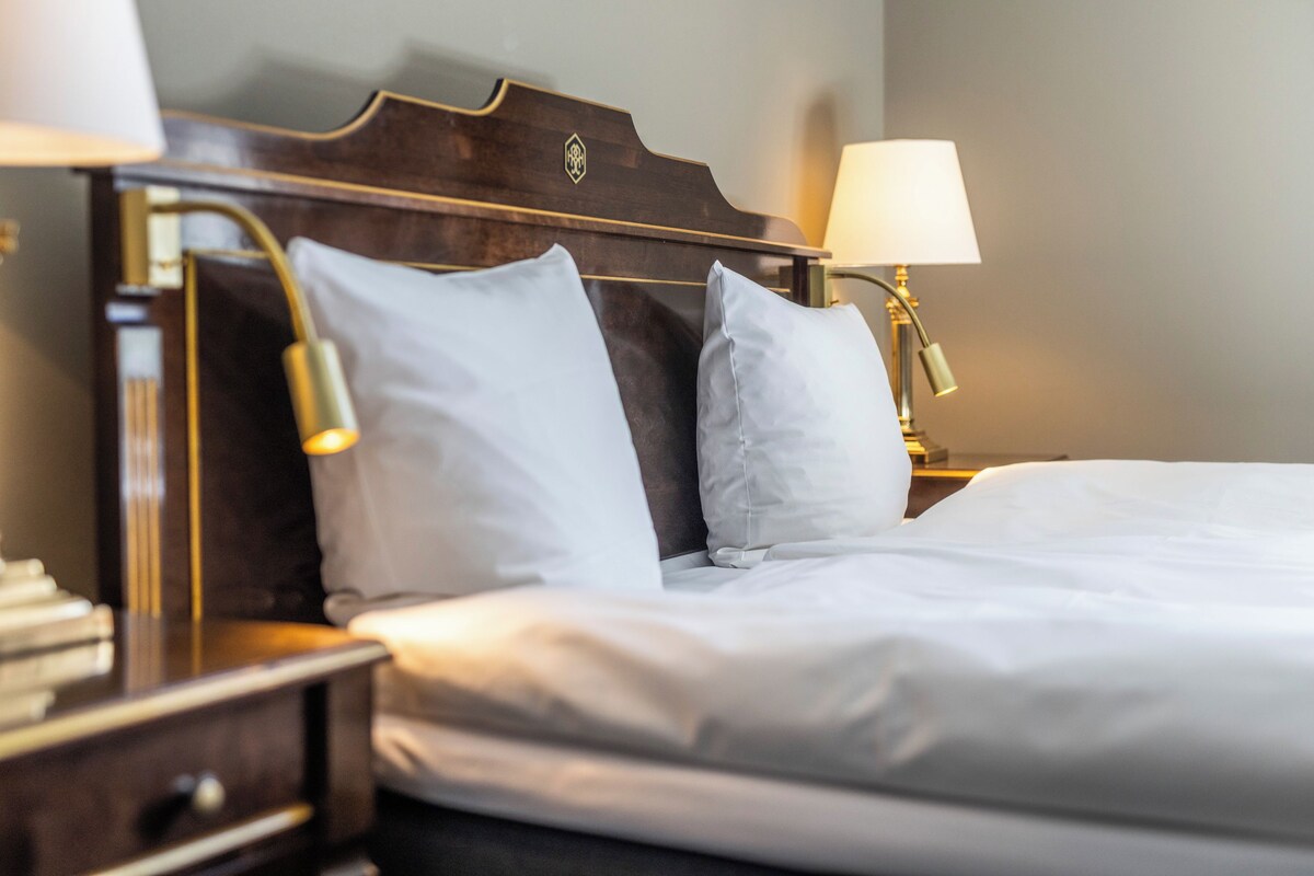 A neatly made bed with white linens, a wooden headboard, and two bedside lamps.