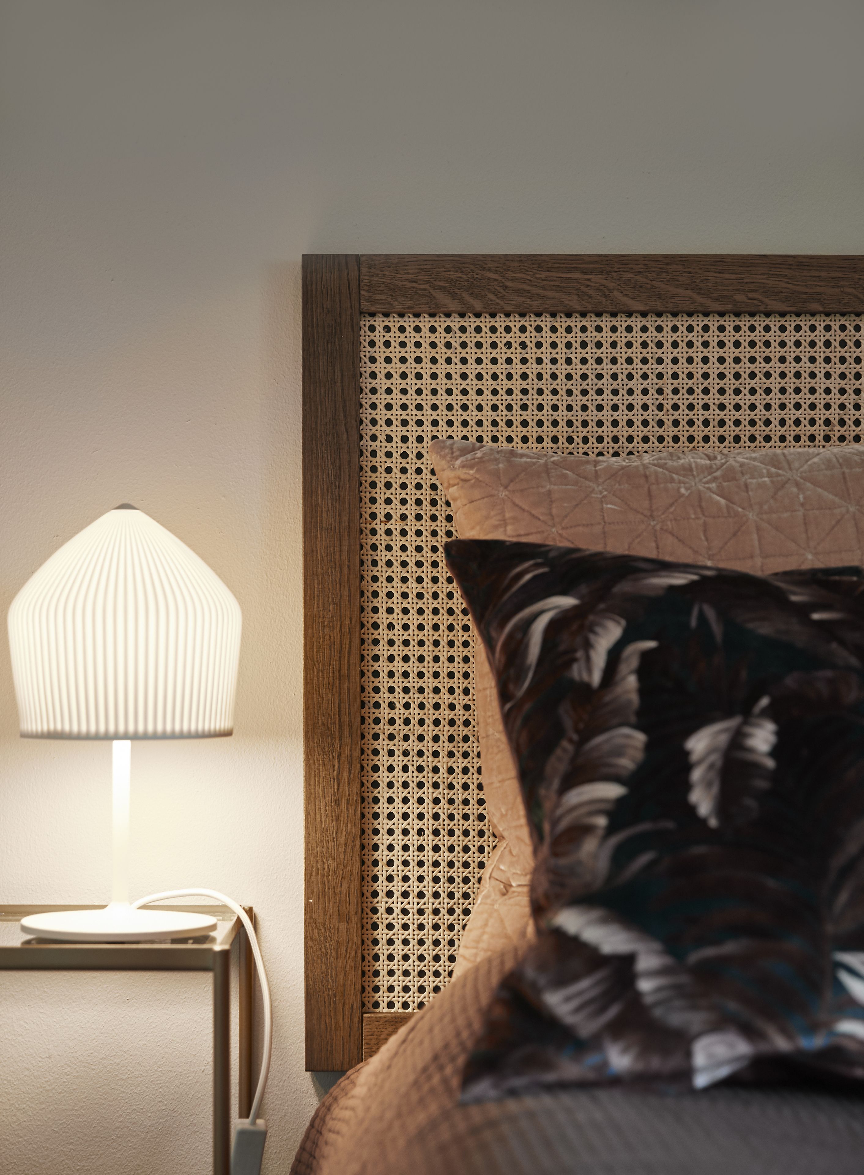 Una cama con cabecera de madera, una lámpara de noche y un cojín estampado con flores.