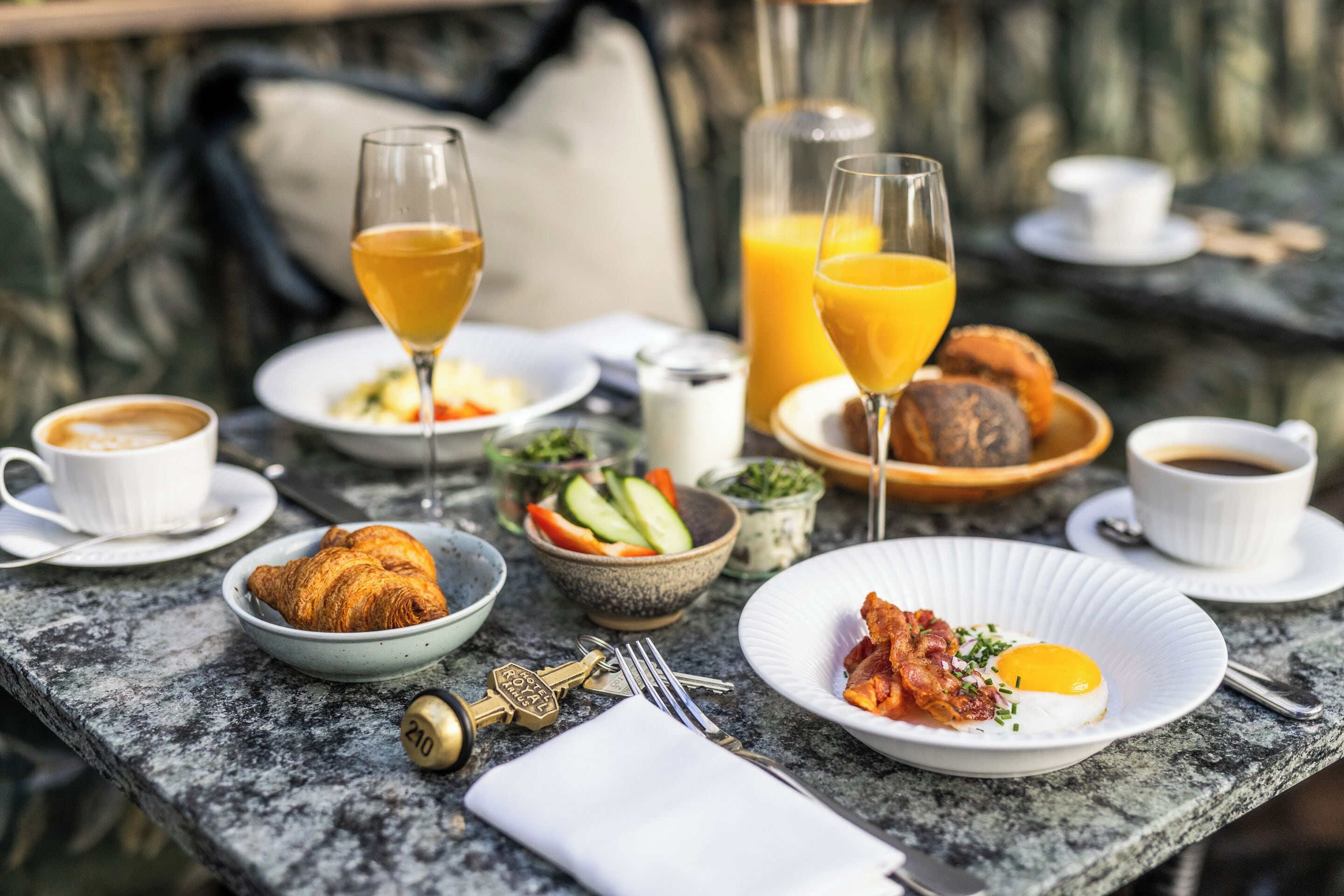 Desayuno con cruasanes, huevos, tocino y jugo en una mesa de mármol.