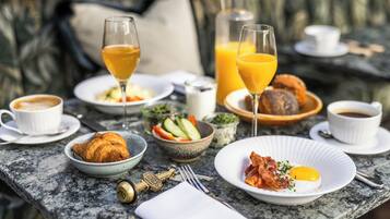 Desayuno con cruasanes, huevos, tocino y jugo en una mesa de mármol.