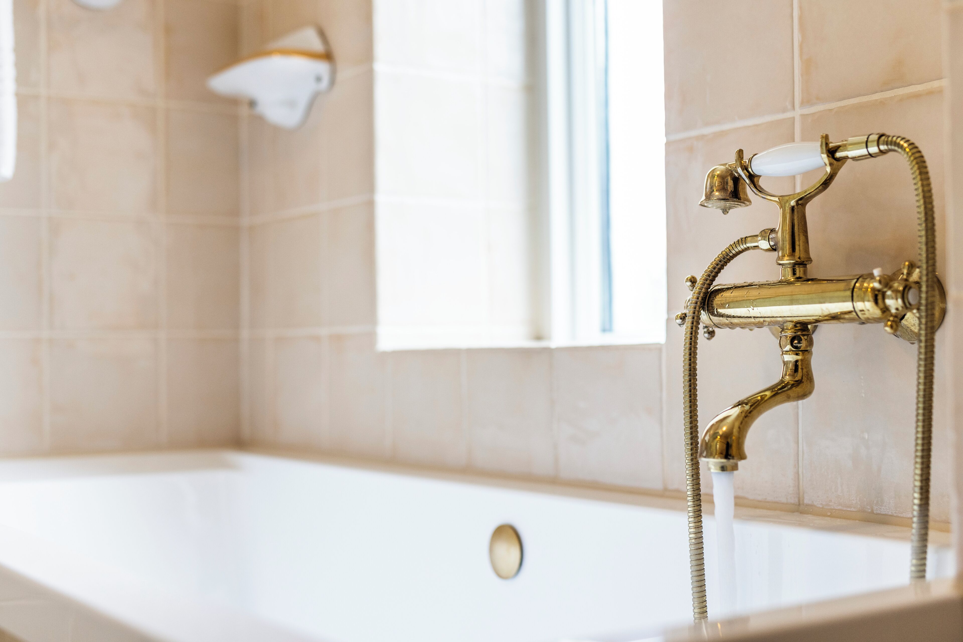 Ein Badezimmer mit Badewanne, einer weißen Wandleuchte und einem Fenster.