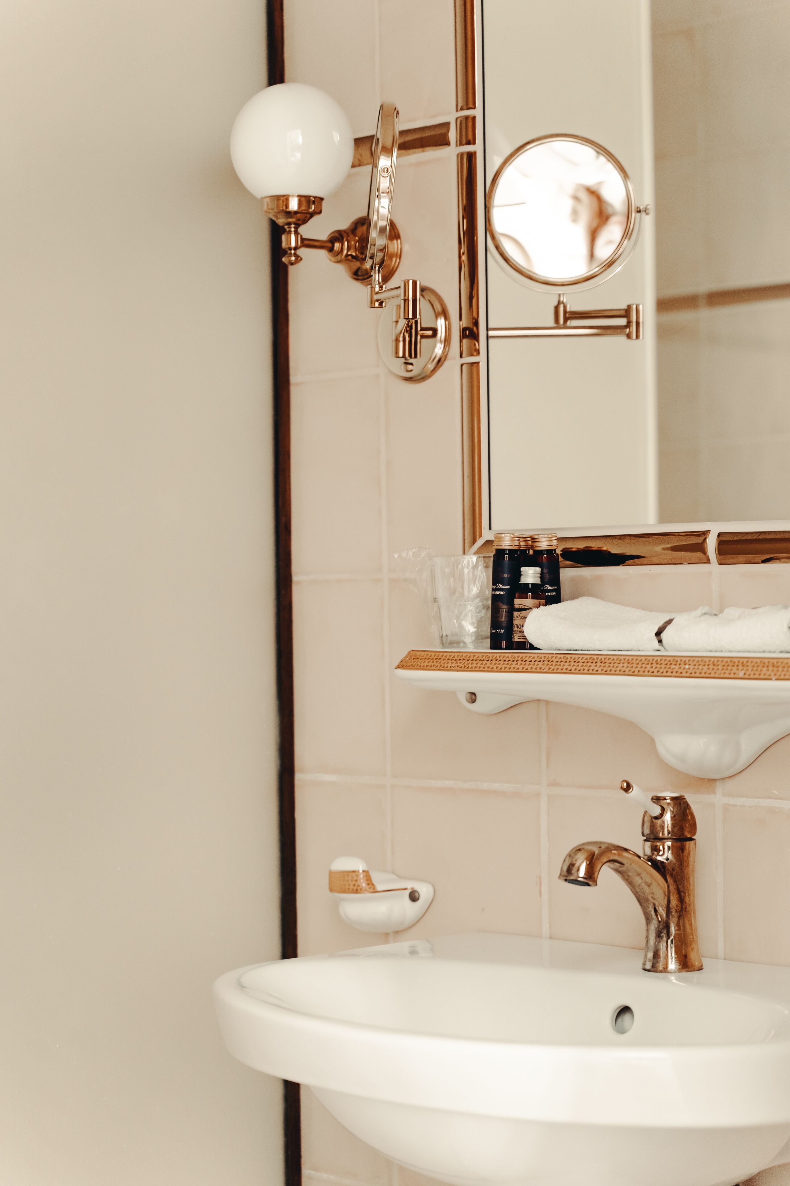 Une salle de bain avec un lavabo blanc, des robinetteries dorées, un miroir et une étagère contenant des articles de toilette.